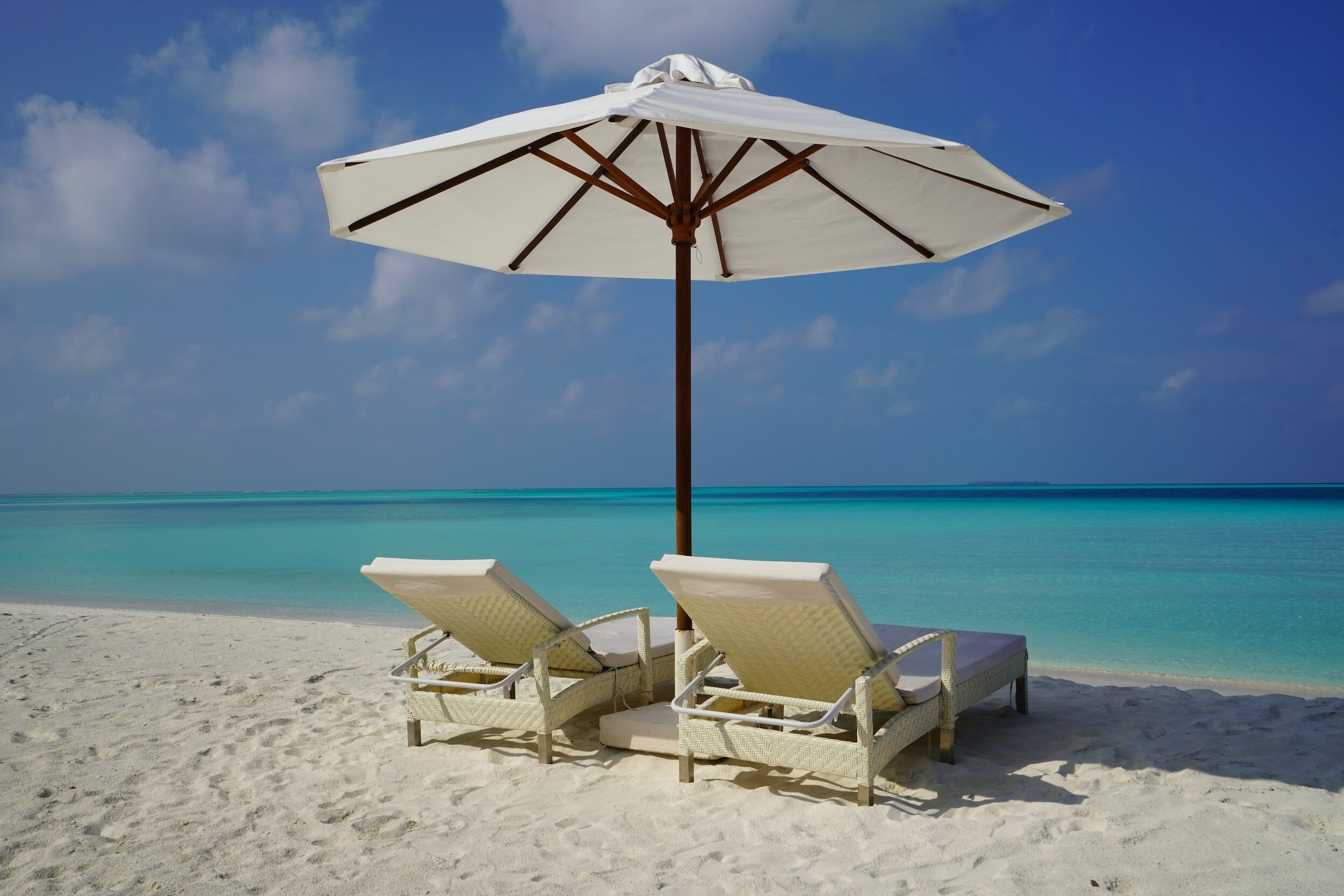 Two lounge chairs under an umbrella on a beach