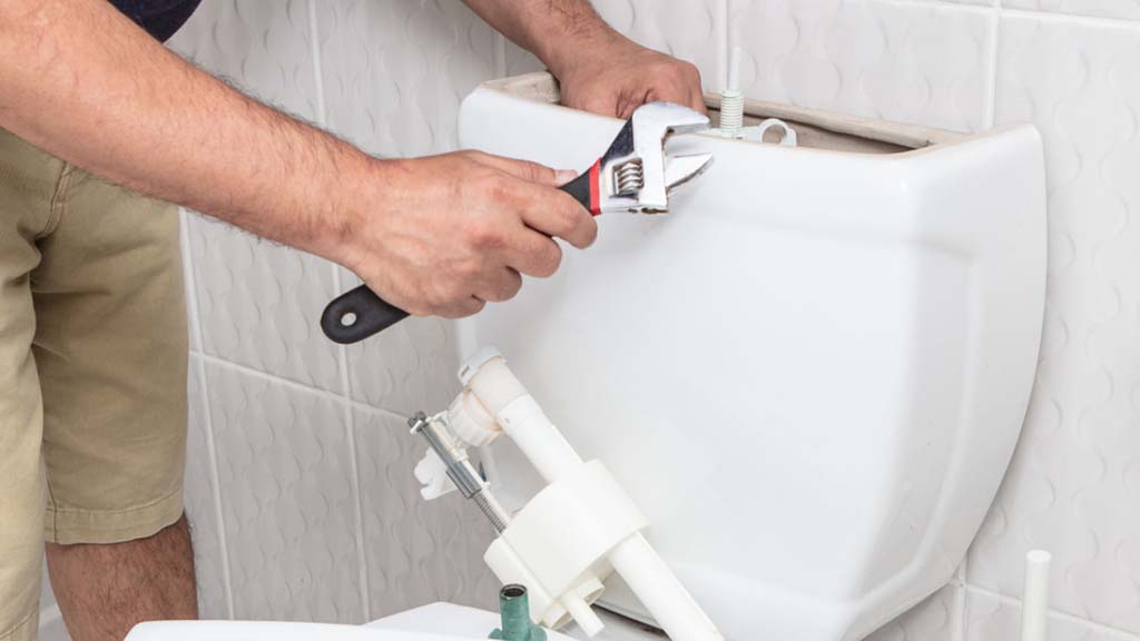 A man using a wrench to fix a toilet
